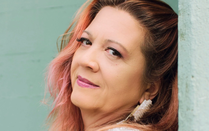 A portrait of the artist leaning back against a colorful wall.